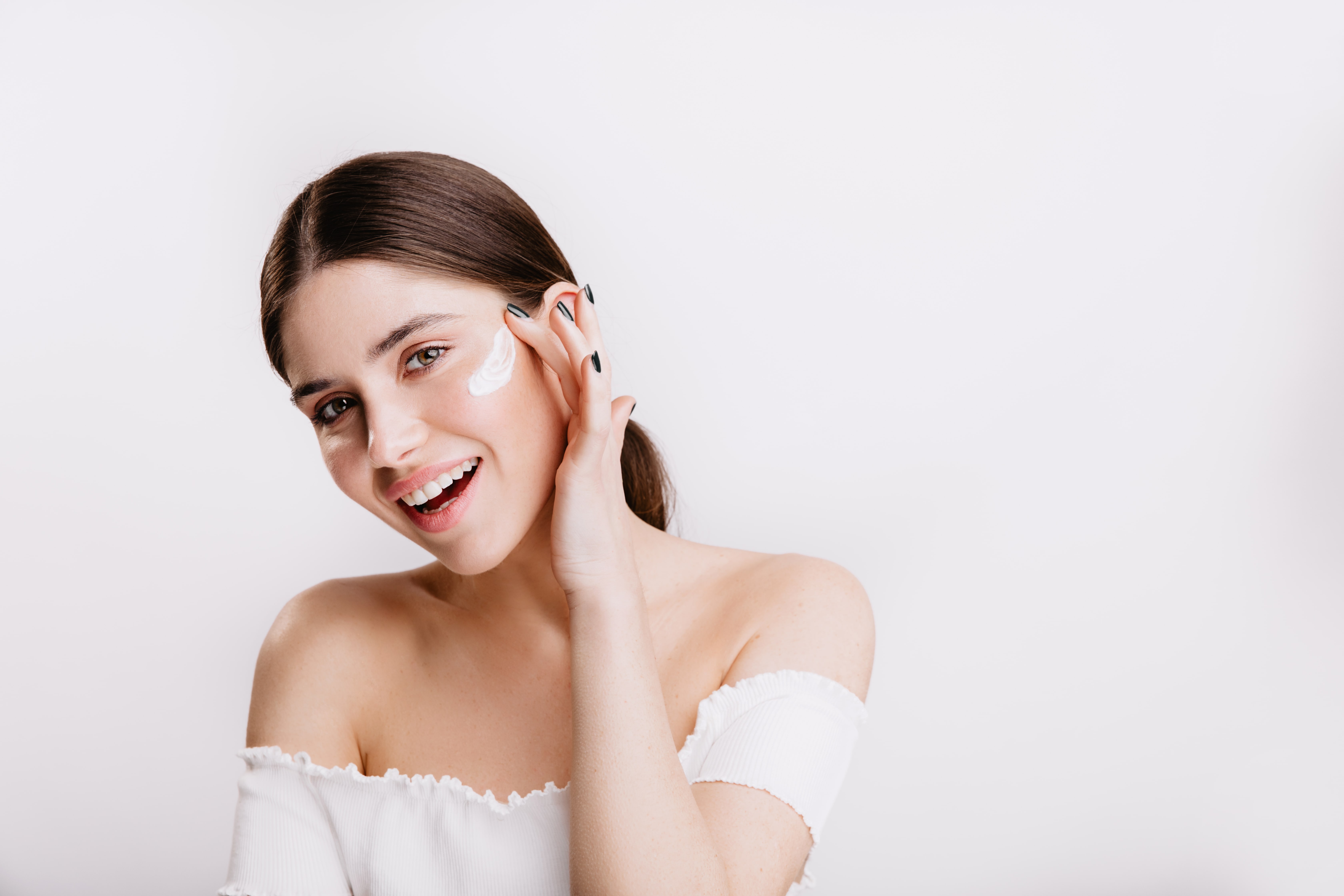 smiling woman puts cream on her face